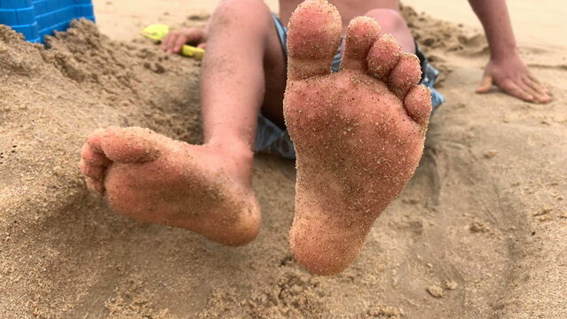 Child moving feet feeling happy at beach, infant foot and toes at shore