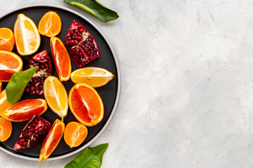 Plate full of fresh citrus fruits with green leaves, top view