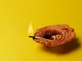 Traditional terracotta or earthen oil lamp on bright yellow background. Indian religious or festive object.