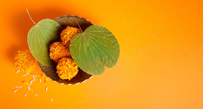 Dussehra greeting card photo background with clear space for message. Top view of a Dussehra leaves and marigold flower in a bowl on saffron color background.