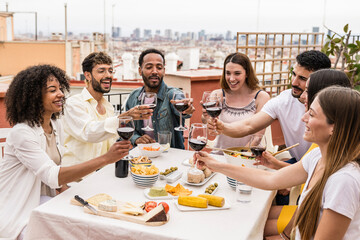 Happy group of friends toasting with wine glasses in a terrace. Diverse group of young people drinking in a rooftop dinner.