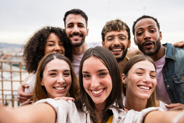 Diverse cheerful group of friends taking a selfie in a rooftop party.Multiracial young happy people smiling while taking a picture in a terrace.