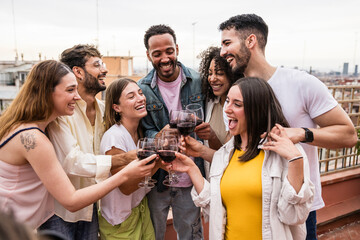 Cheerful carefree group of friends standing and toasting with wine glasses in a terrace.Diverse group of young people celebrating and drinking wine in a rooftop dinner.