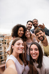Multicultural cheerful group of carefree friends taking a selfie in a rooftop party.Multiracial beautiful young happy people smiling while taking a picture in a terrace.