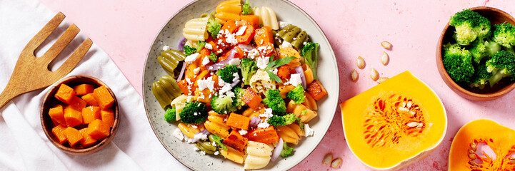 Autumn pasta salad with roasted pumpkin, broccoli, feta cheese on bright light gray background, vivid colors fall season salad, autumn food concept, top view