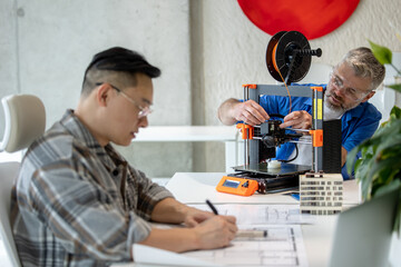 Architects working with 3D printer and projecting house model, drawing blueprint.
