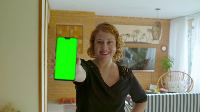 A caucasian woman reveals a green screen phone while smiling