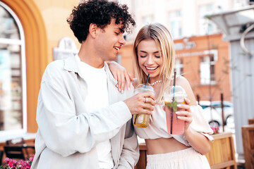 Young smiling beautiful woman and her handsome boyfriend in casual summer clothes. Happy cheerful family. Female having fun. Couple posing in street. Holding and drinking cocktail drink in plastic cup
