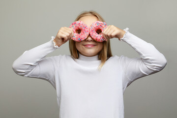 Cheerful happy little child girl having fun with donut on white studio wall background