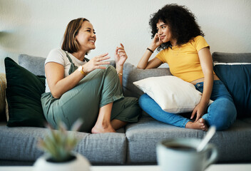 Women, friends relax and conversation in a home with gossip, discussion and happy in a living room. Couch, smile and female person on sofa with communication together in a house lounge with speaking
