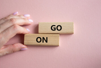 Go on symbol. Wooden blocks with words Go on. Businessman hand. Beautiful pink background. Business...