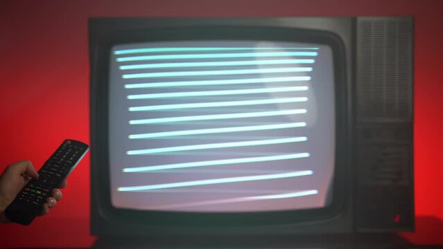 Old broken retro TV with blinking screen on red background, person changing channels with remote control searching for better transmission signal, vintage TV on red background