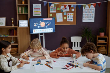 Diverse group of little children doing arts and crafts sitting at table in preschool class, copy space