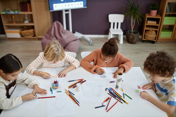 Top view at multiethnic group of children doing arts and crafts sitting at table in preschool...