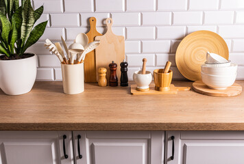 A set of various kitchen tools, utensils made of environmentally friendly materials on the kitchen countertop, a white brick wall. Eco-interior.
