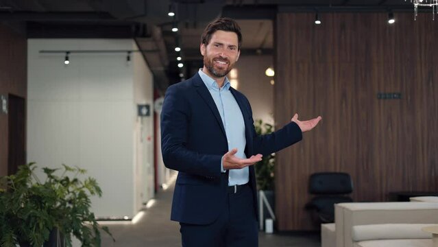 Handsome bearded man inviting to visit successful financial company while standing at hall. Smiling director wearing formal clothes showing sincerity with gesture of invitation. Concept of occupation.