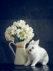 Cute rabbit near jug of fresh flowers