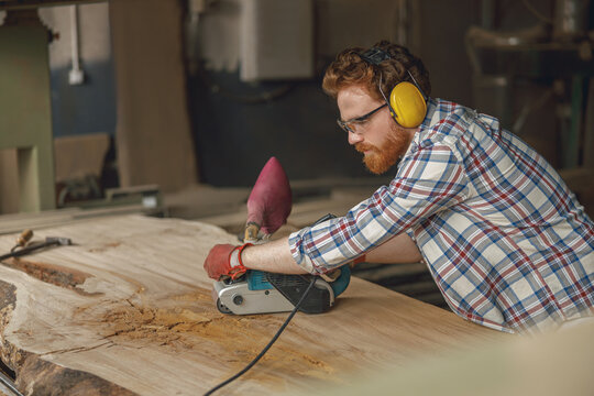 Bearded male wood worker using electric sander for wood. Carpentry workshop. High quality photo