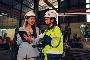 Chief Engineer and Project Manager Wearing Safety Vests and Hard Hats, Use Digital Tablet Computer in Modern Factory, Talking and planning optimization of production.