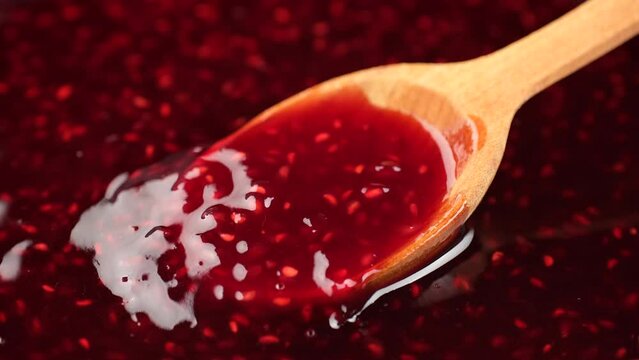 Cooking raspberry jam, close up. Stirring raspberry jam with wooden spoon