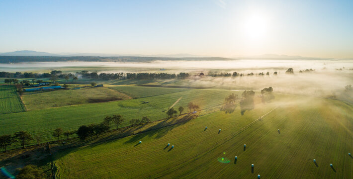 Panorama of green farmland in morning light with mist over river