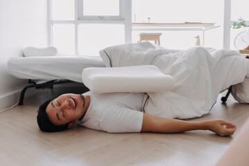 Asian man sleeping lying on floor, having good dream, fall from white bed at home.