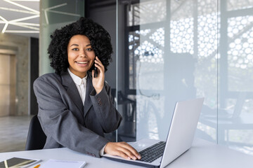 Portrait of a smiling young African American businesswoman working in the office on a laptop and talking on the phone.