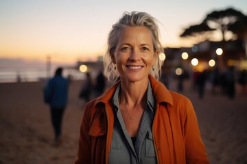 Portrait of happy senior woman looking at camera and smiling while standing against a sunset in a paradise beach. Freedom, peace, relax, holiday concept - obrazy, fototapety, plakaty