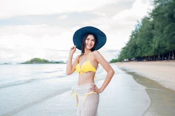 Beautiful woman in yellow bikini on tropical beach. Portrait of happy young woman smiling at sea. Brunette tanned girl in swimwear enjoying and walking on beach.