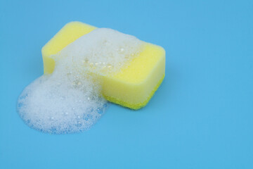 Yellow sponge with white foam on blue background.	