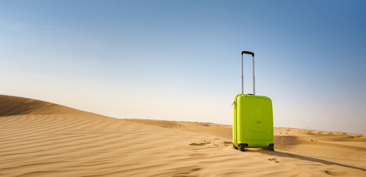 bright light green or yellow suitcase in sands of desert dunes. Concept and idea of travel to United Arab Emirates, Dubai sands at sunset. Summer holiday travel concept