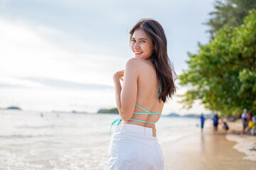 Beautiful woman in blue bikini on tropical beach. Portrait of happy young woman smiling at sea. Brunette tanned girl in swimwear enjoying and walking on beach.