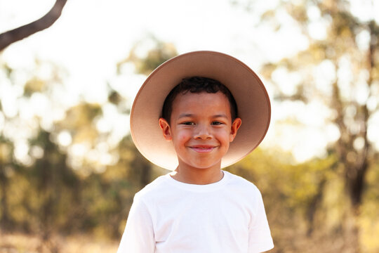 Portrait of happy aboriginal boy wearing hat for sun protection with bokeh bushland background