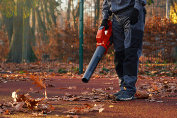 Unrecognizable maintenance man wearing blue uniform and gloves, working with portable leaf blower...
