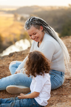 Happy aboriginal mum with daughter sitting on cliff edge in country telling stories