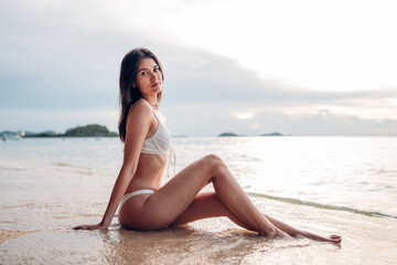 Beautiful caucasian woman in white bikini on tropical beach. Portrait of dark skinned woman smiling...