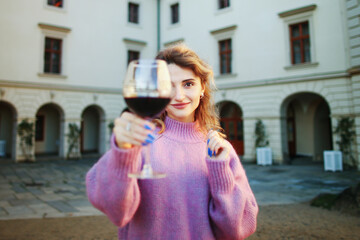 Cute girl with wavy hair holding a glass of wine in her hand covering part of her face.