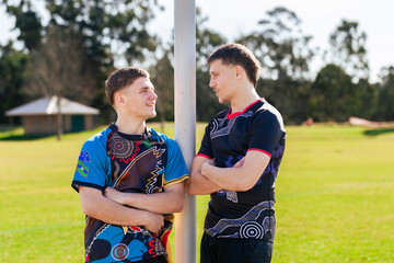 Two teen sports players who are cousins together on football field by goal post