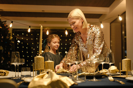 Portrait of mature woman and girl wearing fancy outfits preparing to celebrate Christmas finishing dining table setting