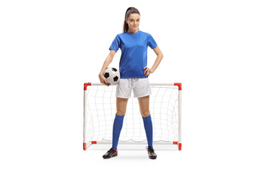 Full length portrait of a female football player with a ball in front of a mini goal