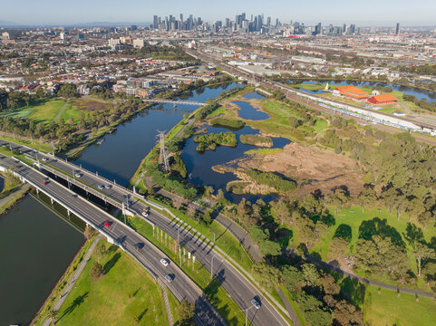 Aerial view a double lane bridge crossing an inner city river alongside green wetlands