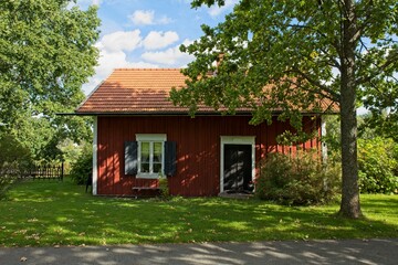 Red painted wooden house and trees in summer.