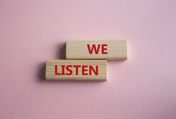 We listen symbol. Wooden blocks with words We listen. Beautiful pink background. Business and We...