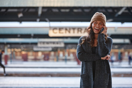 Asian woman laughing whilst waiting at train station with mobile phone