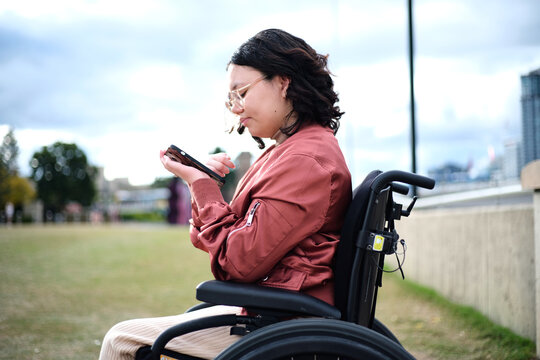 Close Up Shot Of A Woman With Disability Sitting In A Wheelchair While Looking At Her Mobile Phone