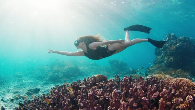 Young woman swims in the ocean. Female freediver glides underwater over the coral reef