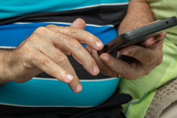 Detalhe das mãos de um homem idoso que está usando um telefone celular.