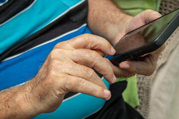 Detalhe das mãos de um homem idoso que está usando um telefone celular.