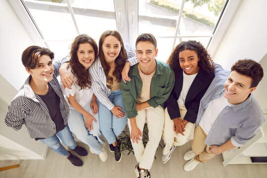 Top View Of A Group Of Happy Smiling Friends High School Students Standing Together And Looking Cheerful And Positively At The Camera In Hallway. Portrait Of Friendly People Guys And Girls Indoors.