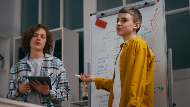 Enthusiastic boys classmates presenting IT project strategy near whiteboard